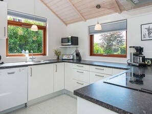 A modern kitchen with white cabinets, a black countertop, and pendant lighting.