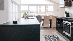 A modern kitchen with a large island, built-in oven, and a view of the city through large windows. - 6 Person Holiday Home in Brovst (Brovst)