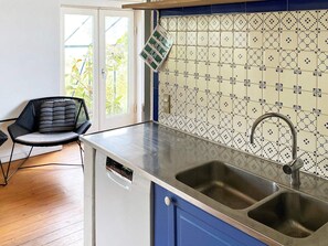 Una cocina con un lavamanos doble, lavavajillas y una silla con cojín a rayas.