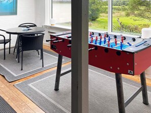 Una habitación con mesa de futbolín, una mesa de comedor con sillas y vistas al exterior.