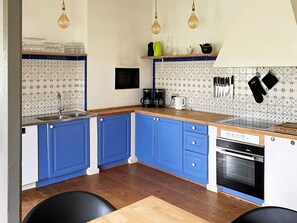 Een keuken met blauwe kastjes, een houten aanrecht, een spoelbak, een koffiezetapparaat en een fornuis.