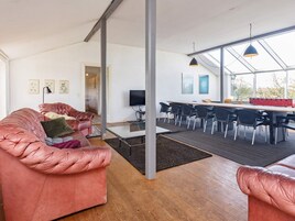 En moderne stue med en lædersofa, et spiseområde med et langt bord og stole, og et stort vindue der lukker naturligt lys ind.