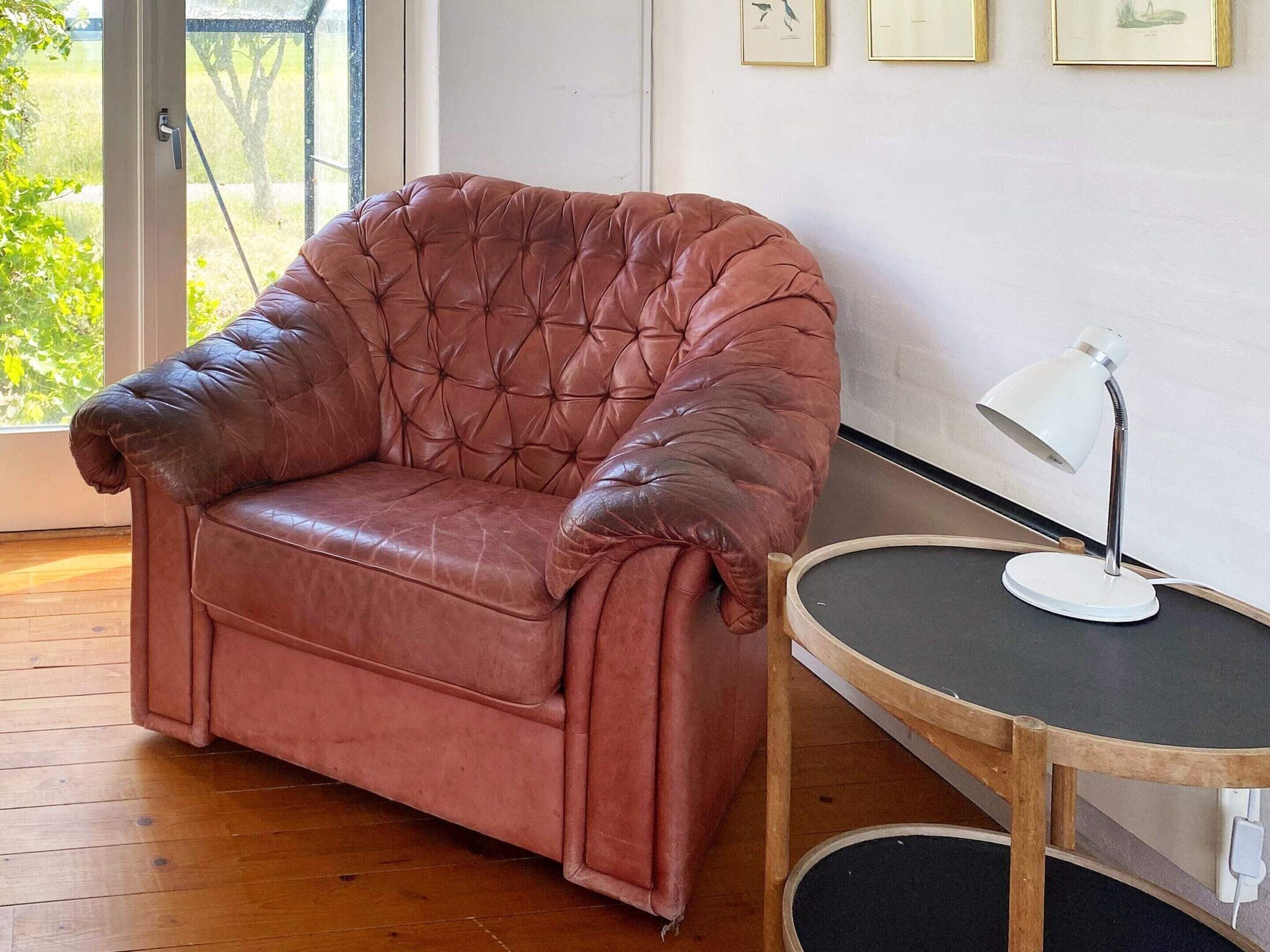 A brown leather armchair with a cushioned backrest, positioned next to a small round table with a white desk lamp.