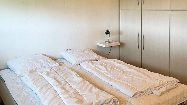 A double bed with a white duvet and pillows, a bedside table with a lamp, and a wardrobe with two doors. - Scenic Retreat in Boddum (Hurup Thy)