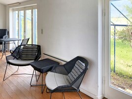 Una habitación con piso de madera, un vidrio que da al exterior y dos sillas de mimbre con cojines.
