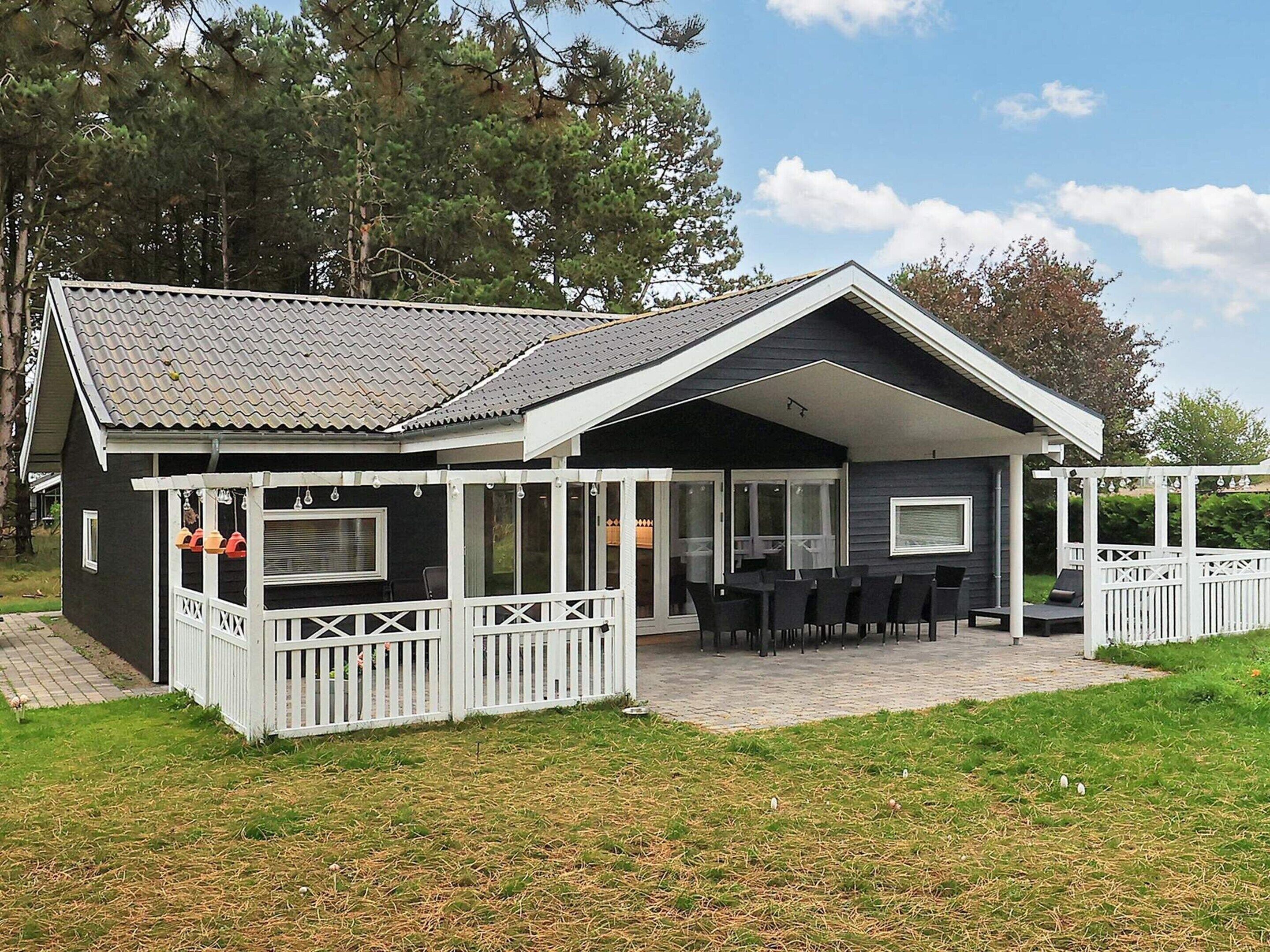 Ein zweistöckiges Haus mit einer überdachten Veranda, einem eingezäunten Deck und einem großen Fenster mit Blick auf den Garten.