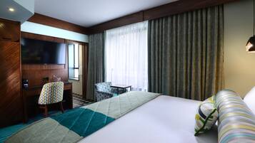 Camera d'albergo con un letto grande, una televisione, una scrivania con sedia e una finestra con tende.