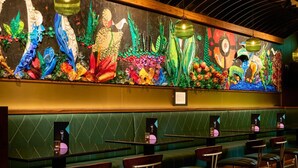 A restaurant with green upholstered booths and tables, a colorful mural on the wall, and hanging green lanterns. - Arthaus Hotel (Dublin)