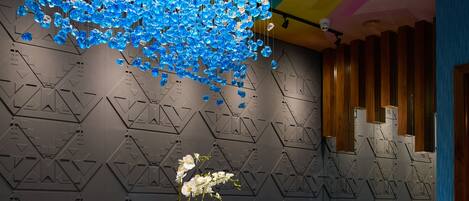 Un área de recepción moderna con un mostrador de mármol, una lámpara de cristal azul colgante y una pared con diseño geométrico.