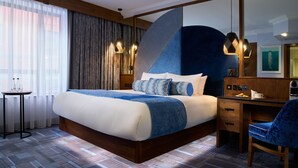 A modern hotel room with a large bed, a desk, and a chair. There is a window with curtains, a wall-mounted lamp, and a painting on the wall. - Arthaus Hotel (Dublin)