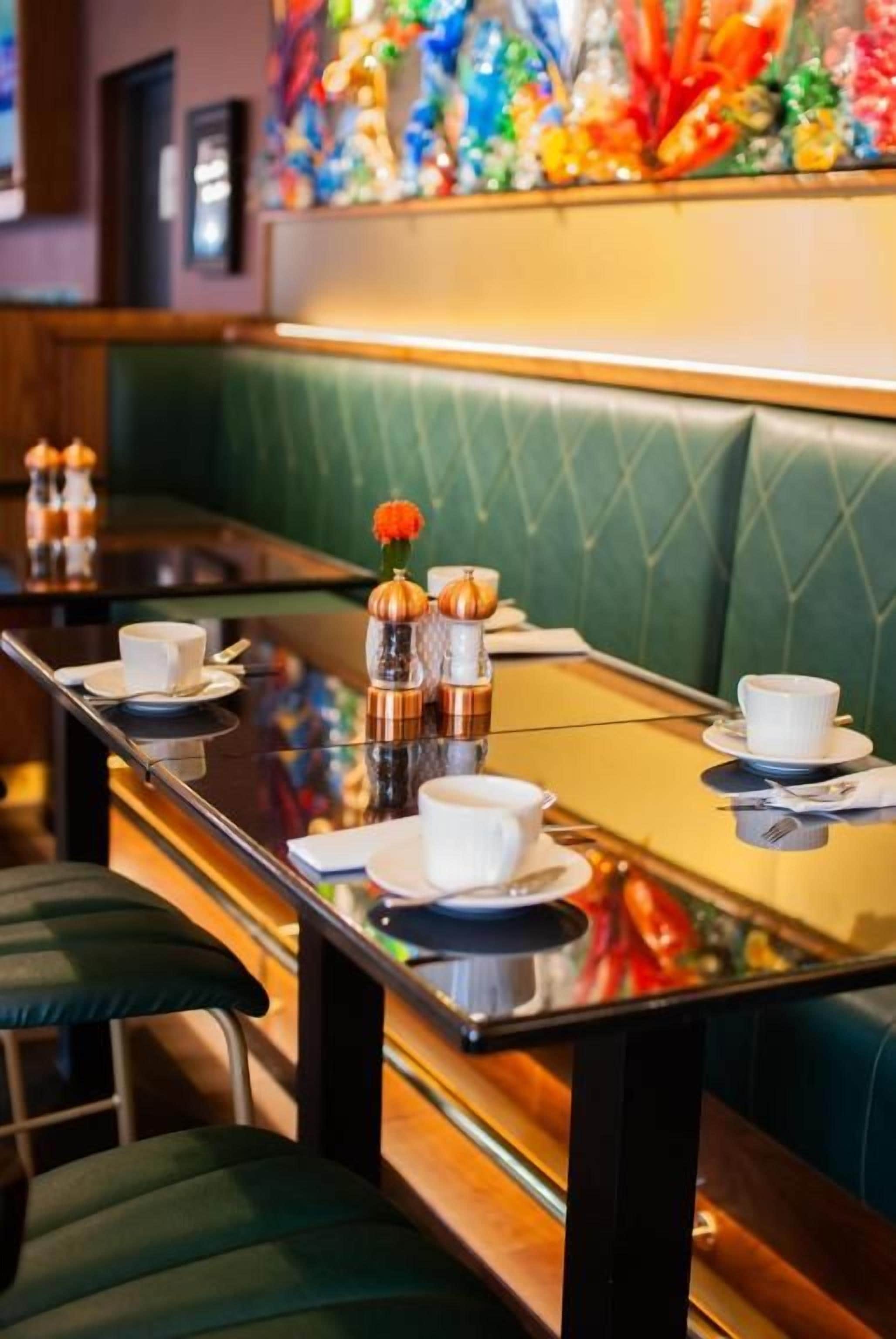 A restaurant booth with a glass table, white plates, and a vase with flowers.
