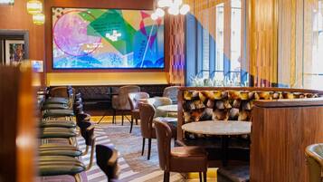 Een restaurantinterieur met een groot scherm waarop een kleurrijke grafiek staat, verschillende zithoeken met zowel zitjes als tafels, en een gedessineerde wand.