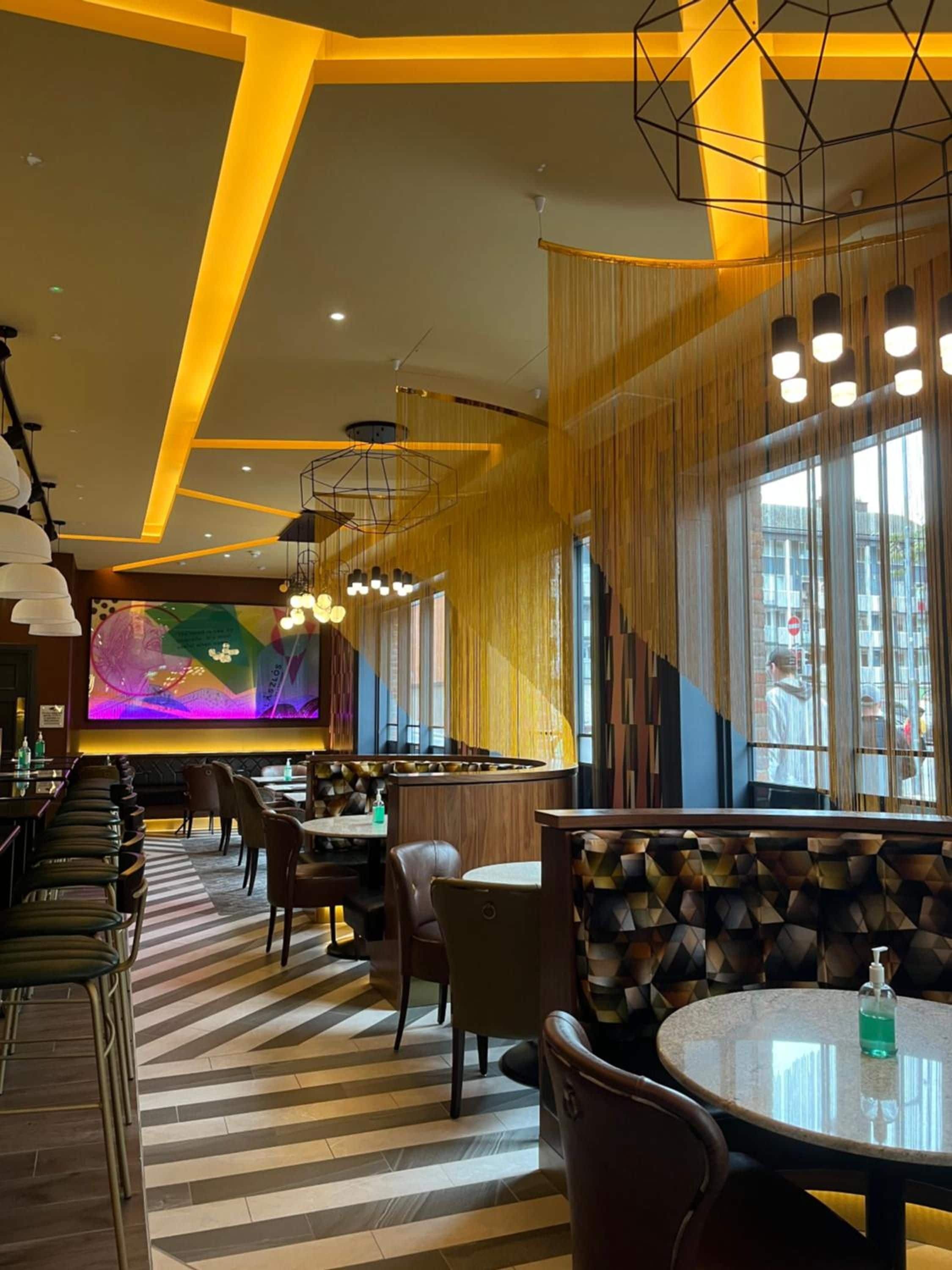A modern interior with a bar area, seating, and a large digital screen displaying colorful content.