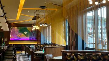 A modern interior with a bar area, seating, and a large digital screen displaying colorful content.