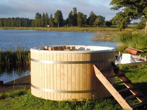 A wooden hot tub with a ladder, surrounded by a grassy area and a body of water. - 4 Person Holiday Home in Hova (Hova)