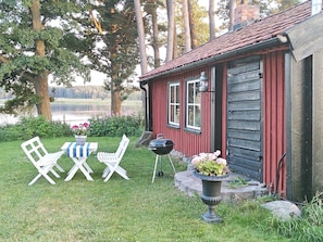 Une cabane en bois rouge, avec une porte noire, des fenêtres à cadre blanc et un petit porche comprenant un banc et une table.