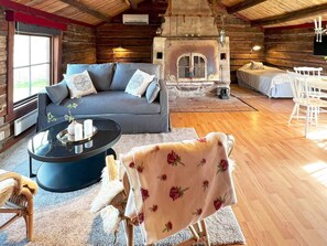 A cozy log cabin interior with a sofa, a round coffee table, a fireplace, and a dining area. - 4 Person Holiday Home in Hova (Hova)