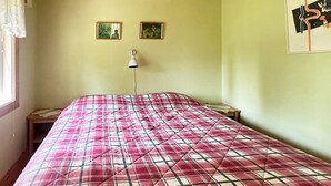 Ein Zimmer mit einem Bett, einem Nachttisch, einer Lampe und zwei gerahmten Bildern an der Wand.