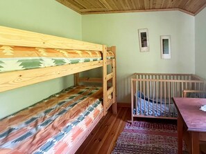 A room with bunk beds and a crib, wooden walls, and a patterned rug. - 4 Person Holiday Home in Braas (Braås)