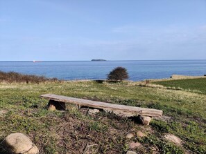 A wooden bench in a grassy area with a view of the sea and a distant island.