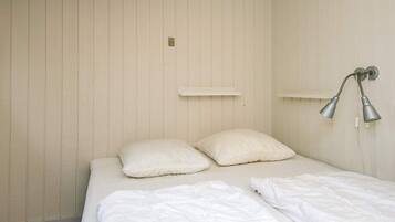 Ein Schlafzimmer mit einem Bett, zwei Kissen, einer weißen Wand und einer Wandleuchte.
