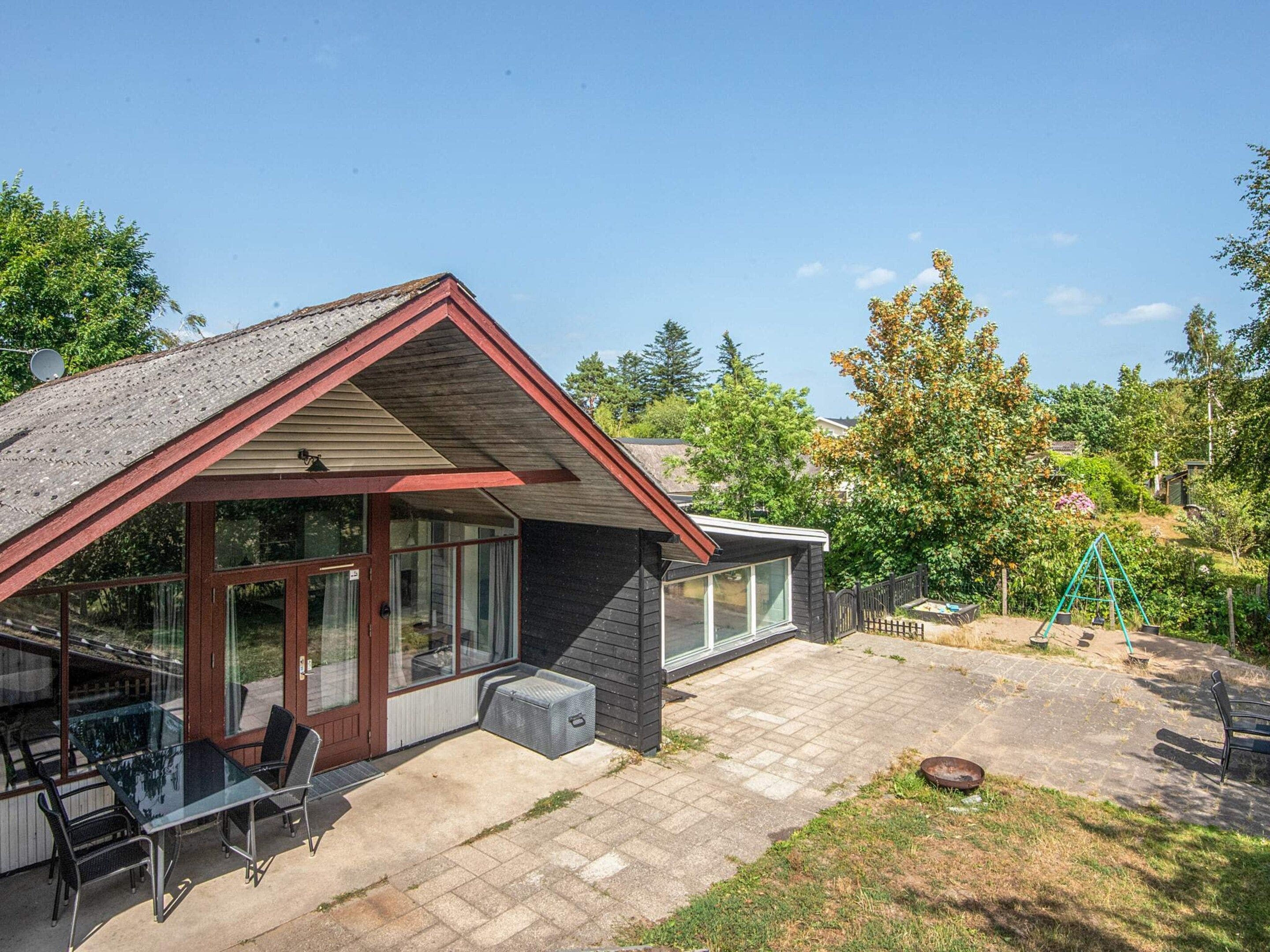A house with a covered patio, a dining area with outdoor furniture, and a fenced backyard with a swing set.