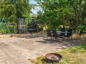 An outdoor patio with a table and chairs, a swing set, and a fire pit.