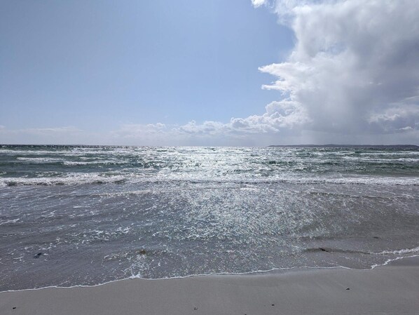 A beach with waves, a clear sky, and a distant landmass.