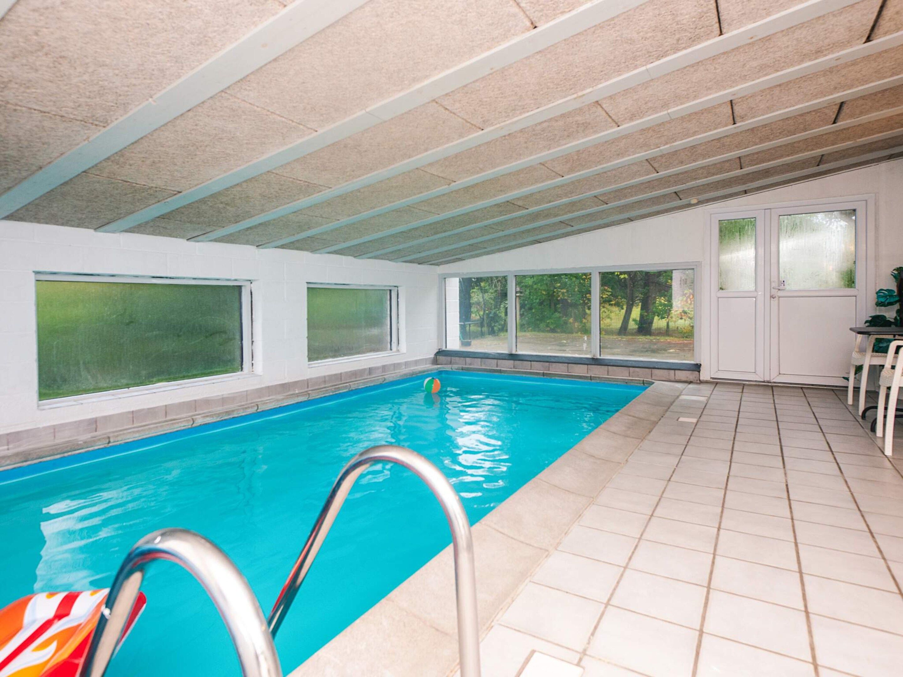Una piscina interior con amplias ventanas de vidrio, suelo de baldosas y una puerta que da al exterior.