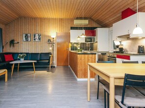 A modern kitchen with wooden cabinetry, a central island, and a dining area with a table and chairs. - 4 Star Holiday Home in Ebeltoft (Ebeltoft)
