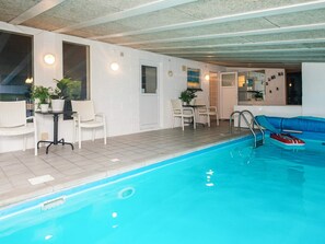 An indoor swimming pool area with a lounge chair, a small table with chairs, and a potted plant. - 4 Star Holiday Home in Ebeltoft (Ebeltoft)