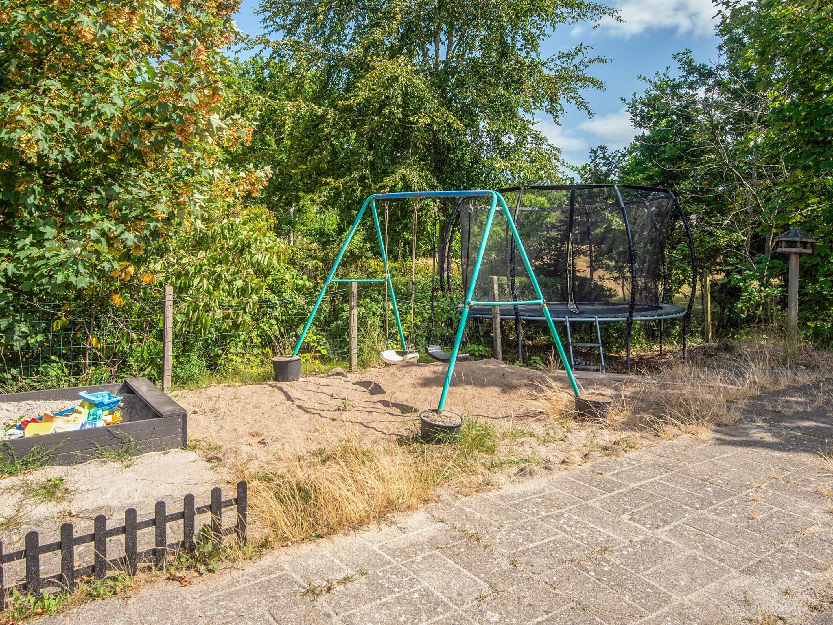 A playground with a swing set and a trampoline, surrounded by trees and a fence.