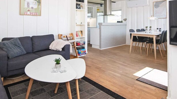 Un salon moderne avec un canapé gris, une petite table blanche et un coin cuisine comprenant une table à manger et des chaises.