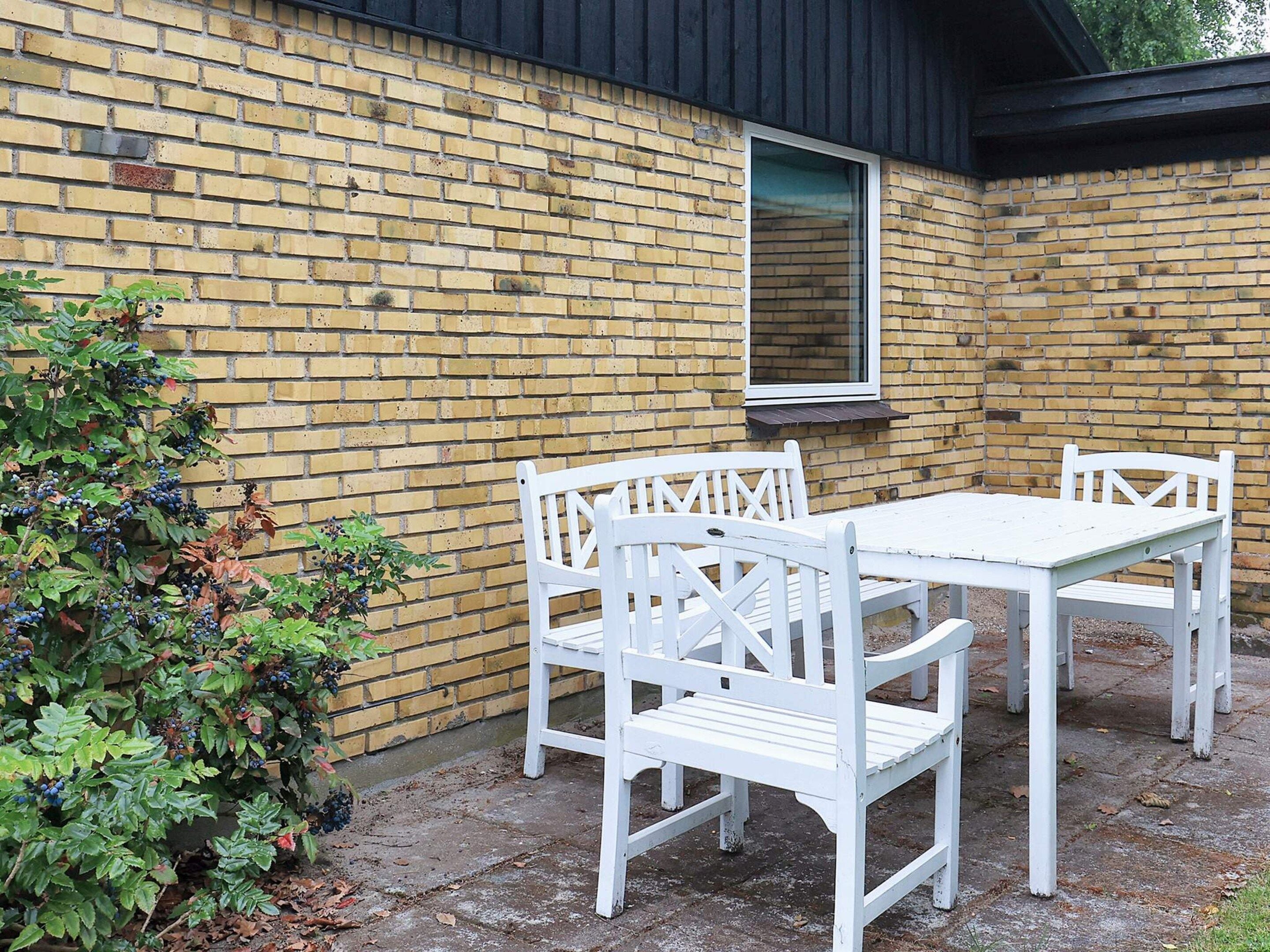 A patio with a white table and chairs, a brick wall, and a window.