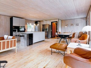 Ett modernt kök med en central köksö, en matplats med stolar och en sittgrupp med en soffa och ett soffbord.