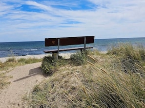 A bench by the beach with the ocean in the background. - 4 Star Holiday Home in Vaeggerlose (Vaeggerlose)