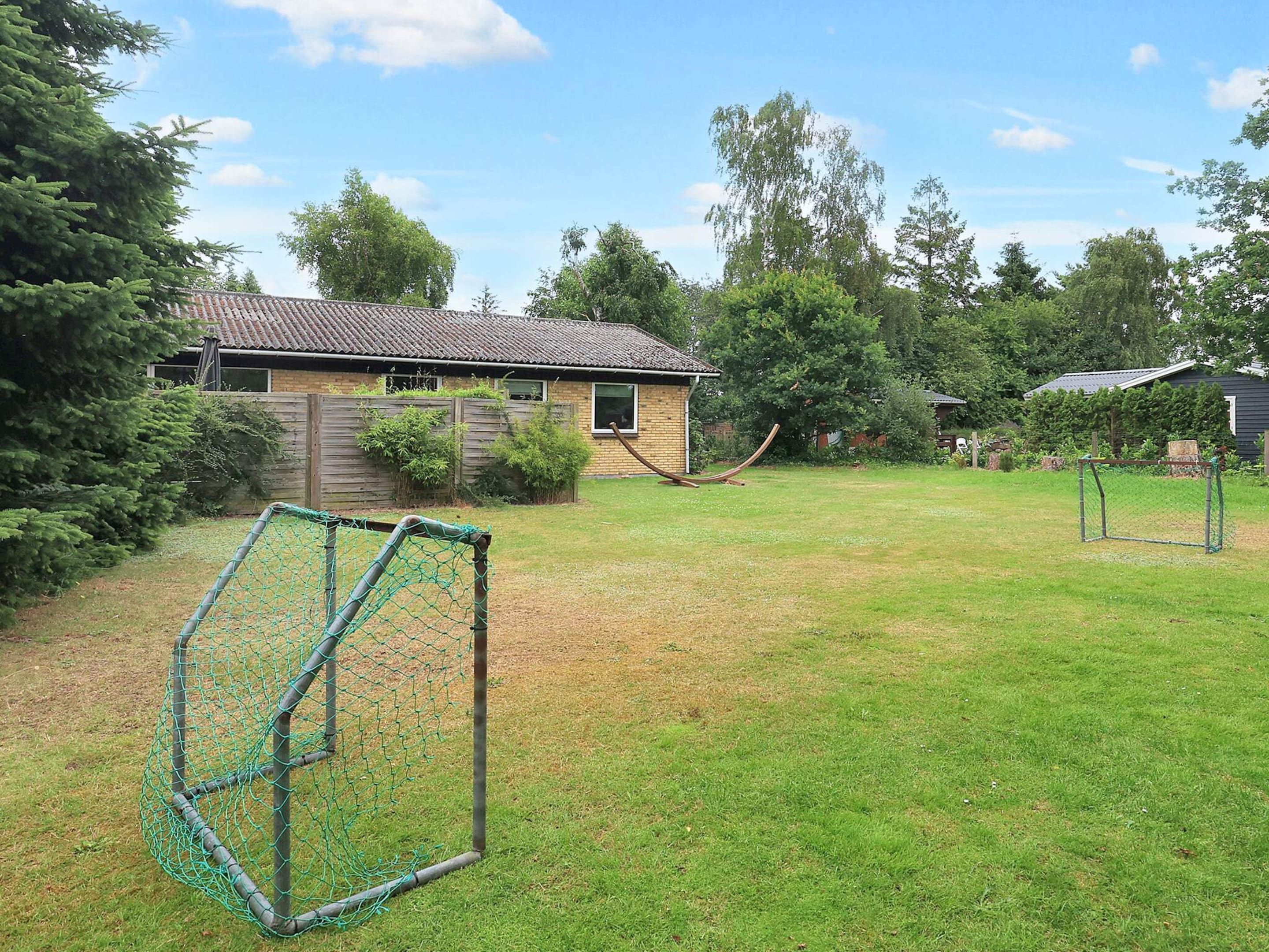 A residential backyard with a fenced play area, a house with a tiled roof, and surrounding greenery.