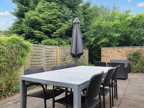 Een terras buiten met een rechthoekige tafel en stoelen, een grijze parasol en een bakstenen muur.