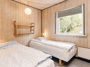 Ett rum med två sängar, ett fönster med utsikt över grönområden och en vägghylla.