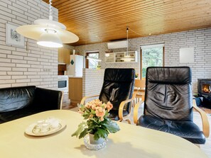 Uma sala de estar moderna com área de jantar, apresentando uma lareira, poltronas de couro e uma mesa com um vaso de flores.