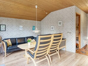 A room with a wooden ceiling, white brick walls, a black leather sofa, a wooden dining table with chairs, and a hanging light fixture.