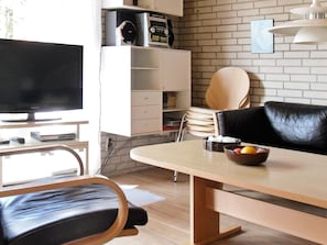 A modern living room with a flat-screen TV, a dining table, a leather chair, and a white cabinet against a brick wall. - 4 Person Holiday Home in Vaeggerlose (Vaeggerlose)