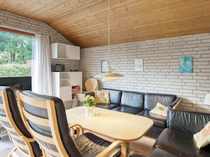 Une pièce chaleureuse avec un plafond en bois, un mur en briques, un canapé, une table à manger et un téléviseur.