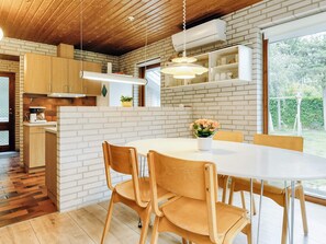A modern kitchen with white brick walls, wooden cabinets, and a dining area with a white table and chairs. - 4 Person Holiday Home in Vaeggerlose (Vaeggerlose)