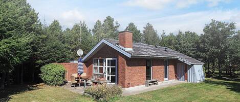 A brick house with a chimney, a patio with a table and chairs, and a small garden.