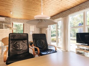 A modern dining area with a wooden ceiling, two leather chairs, a table, and a television on a stand. - 4 Person Holiday Home in Vaeggerlose (Vaeggerlose)