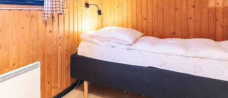 A single bed with a black frame, a wall-mounted heater, and a window with a checkered curtain.