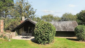 A rustic cabin with a stone chimney, a covered patio with outdoor seating, and a well-maintained lawn. - 4 Star Holiday Home in Rodby (Rodby)