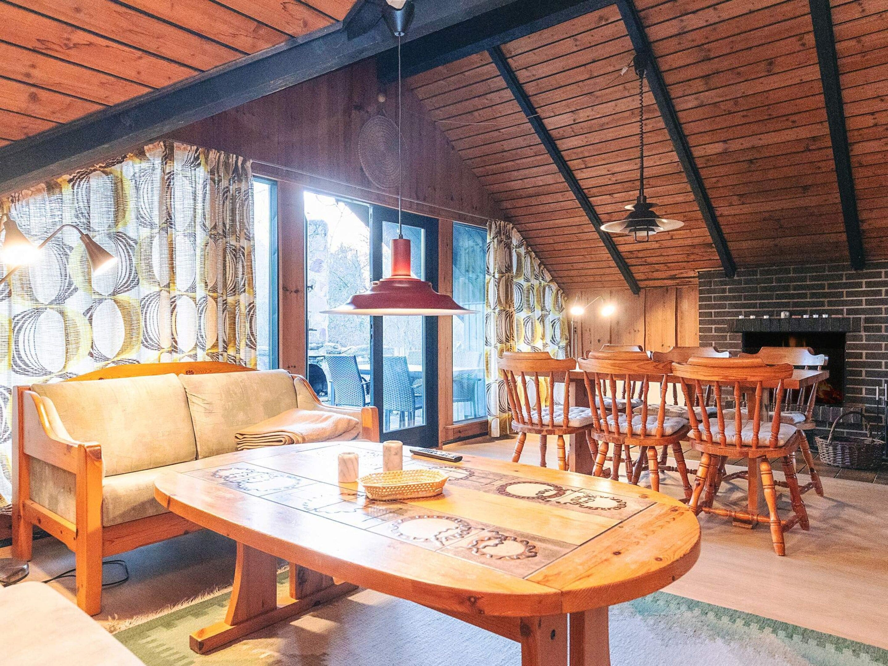 A cozy room with a wooden ceiling, a sofa, a dining table with chairs, and a fireplace.