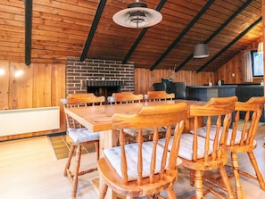 A rustic dining area with a brick fireplace, wooden chairs, and a long table.